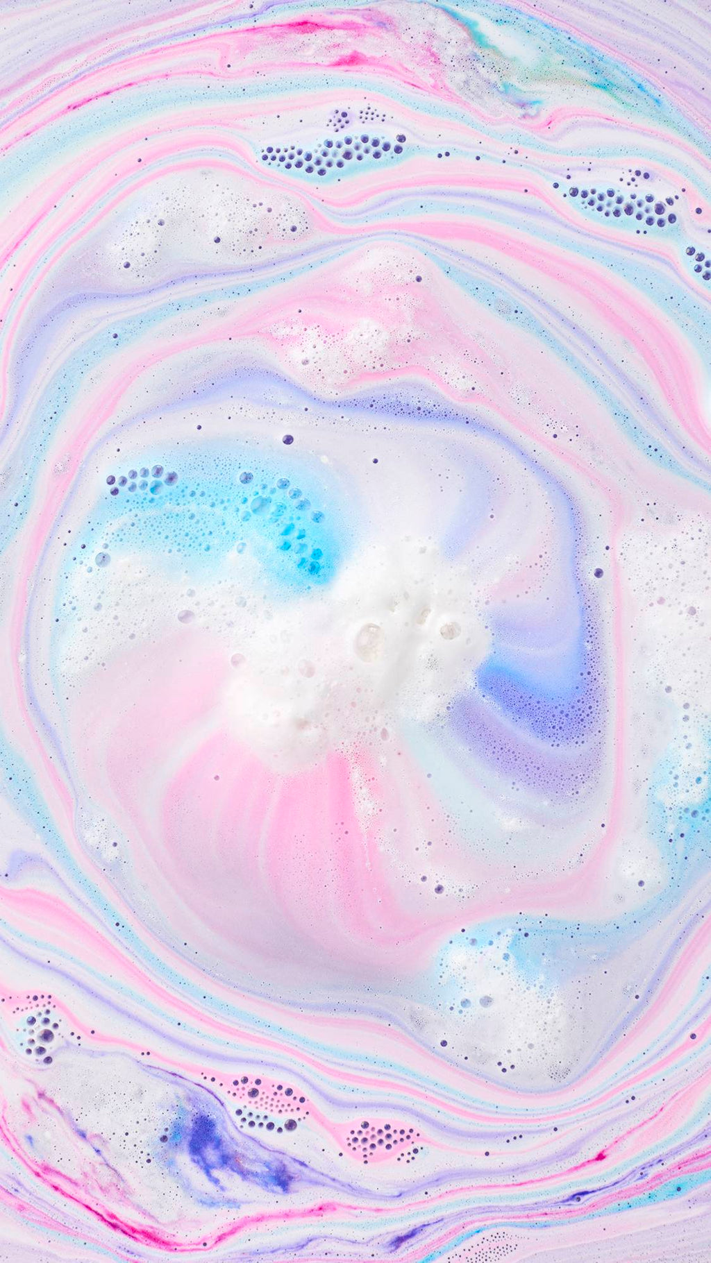 Top-down view of Toby's Magic Cow Bath Bomb dissolving, creating a mesmerizing swirl of pastel pink, blue, and purple foam across the water.