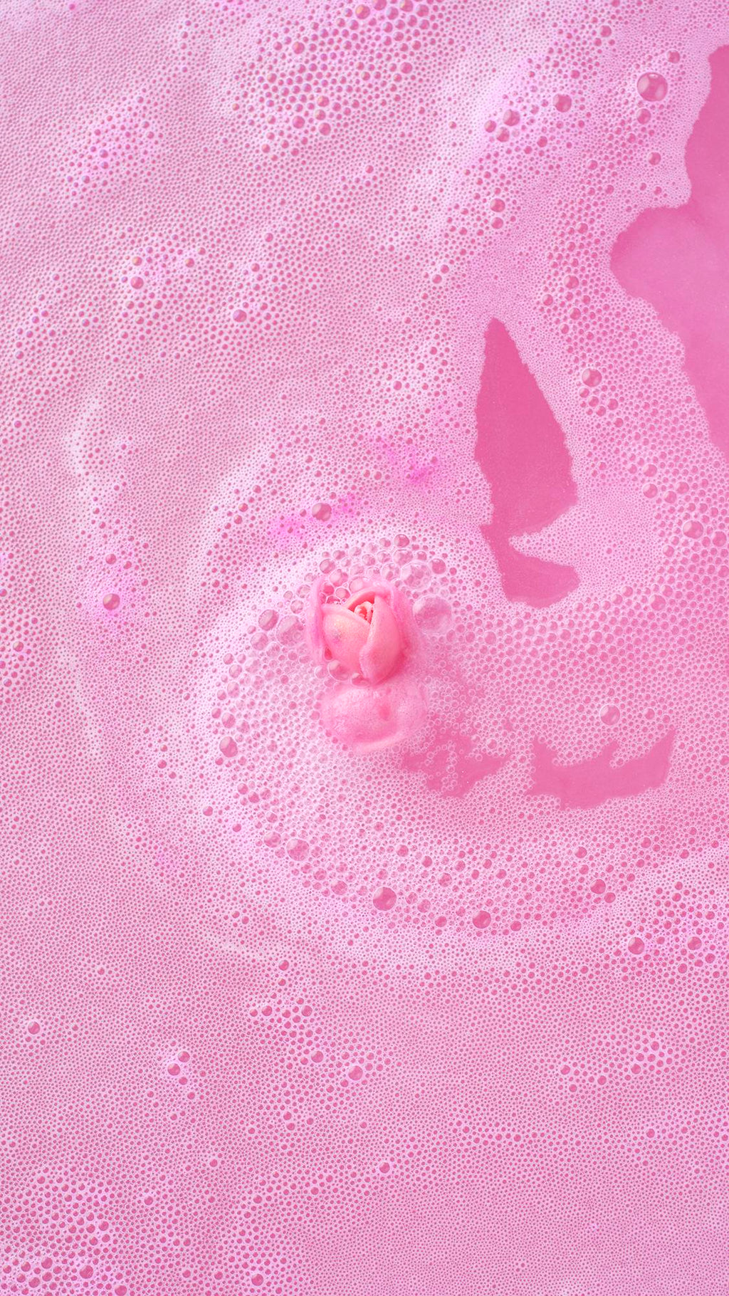 Top-down view of the Sex Bomb Bath Bomb fully dissolved, with its signature pink rosebud floating in the center of thick, frothy pink bathwater.