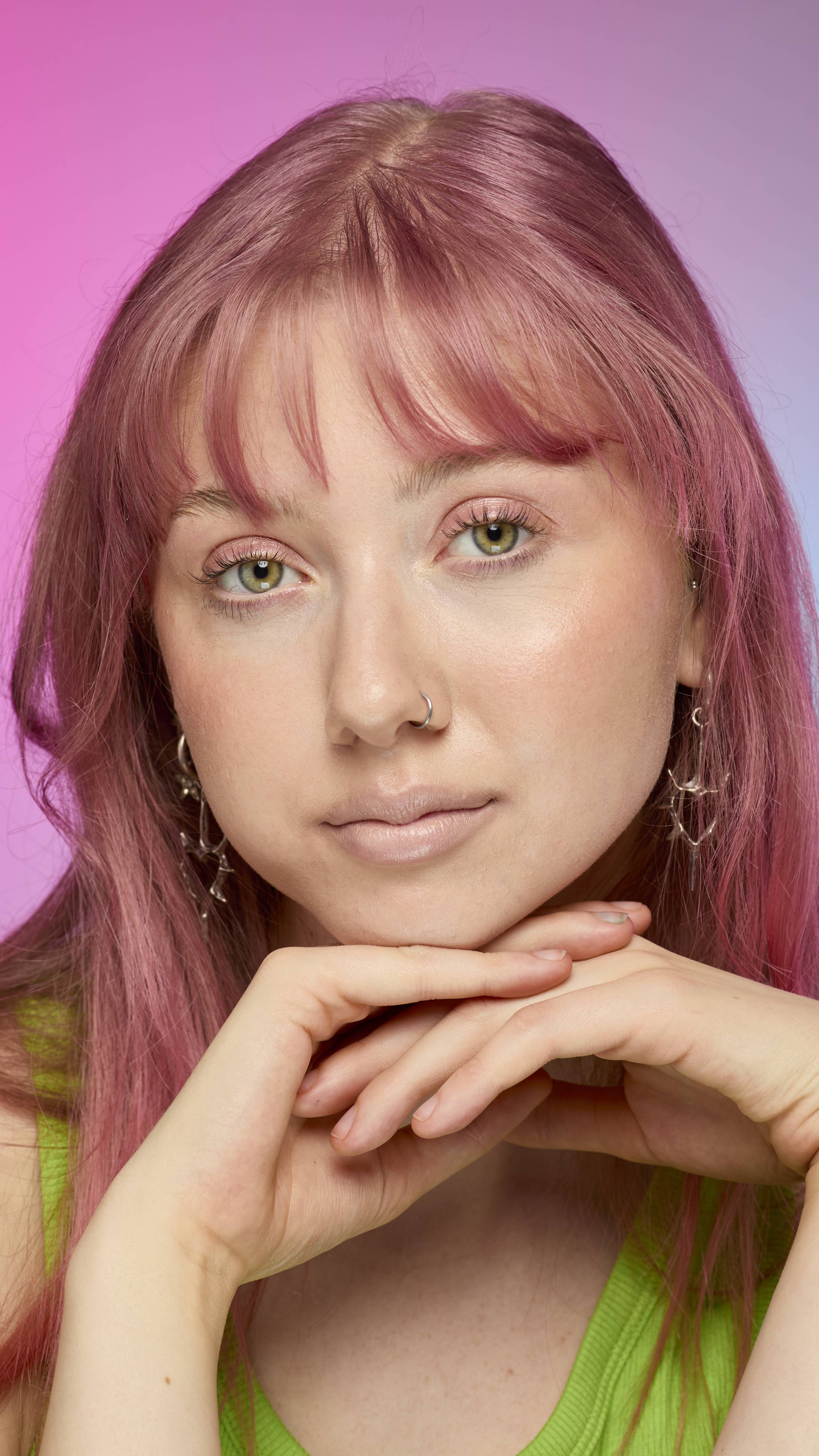 The image shows a fair-skinned model on a pink and blue gradient background. They have pink hair and subtle, peach-nude shimmering lips from using the Peach parfait lip cream.