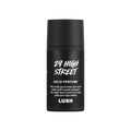 A small, cylindrical black, twist-up tube of Lush '29 High Street' solid perfume. The matte black packaging features white text including the product name, a brief description, and the Lush logo.