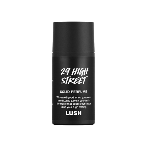 A small, cylindrical black, twist-up tube of Lush '29 High Street' solid perfume. The matte black packaging features white text including the product name, a brief description, and the Lush logo.