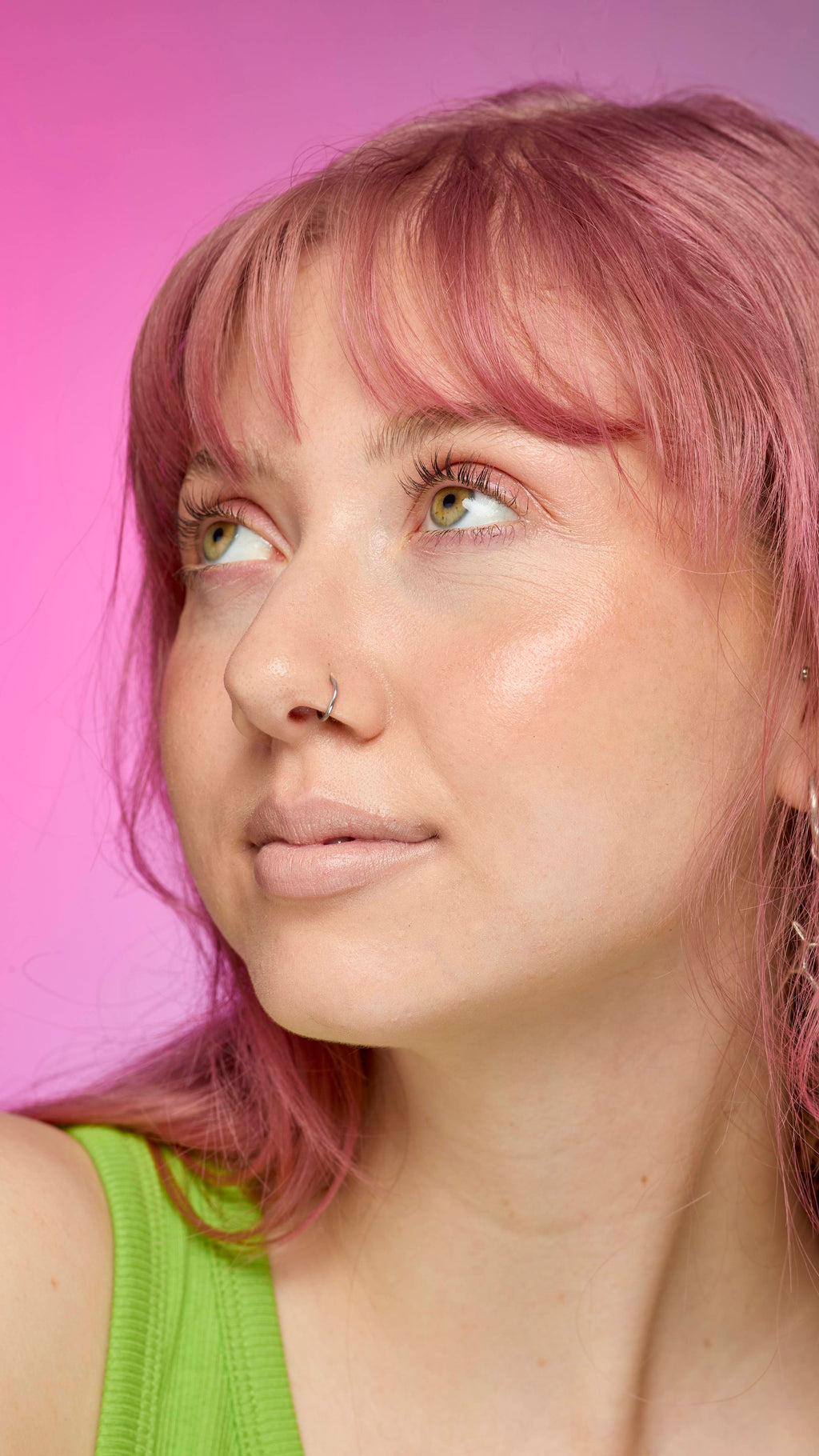 The image shows a fair-skinned model on a pink and blue gradient background. They have pink hair and subtle, peach-nude shimmering lips from using the Peach parfait lip cream.
