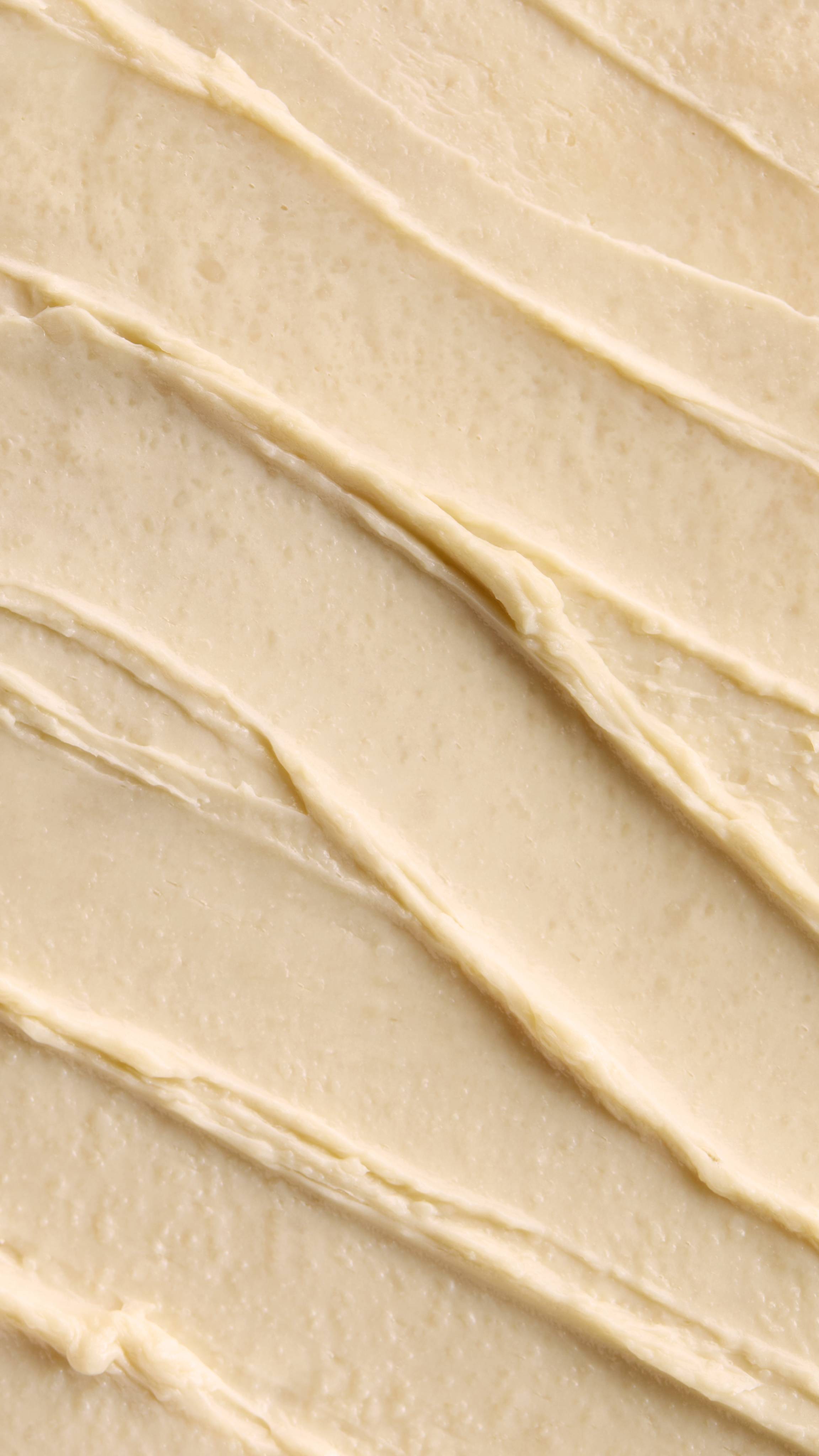 A close-up of a Super Milk Shampoo with distinct, diagonal ridges and soft peaks. The texture suggests a rich, thick consistency, creating a visually pleasing and inviting pattern of smooth swirls.