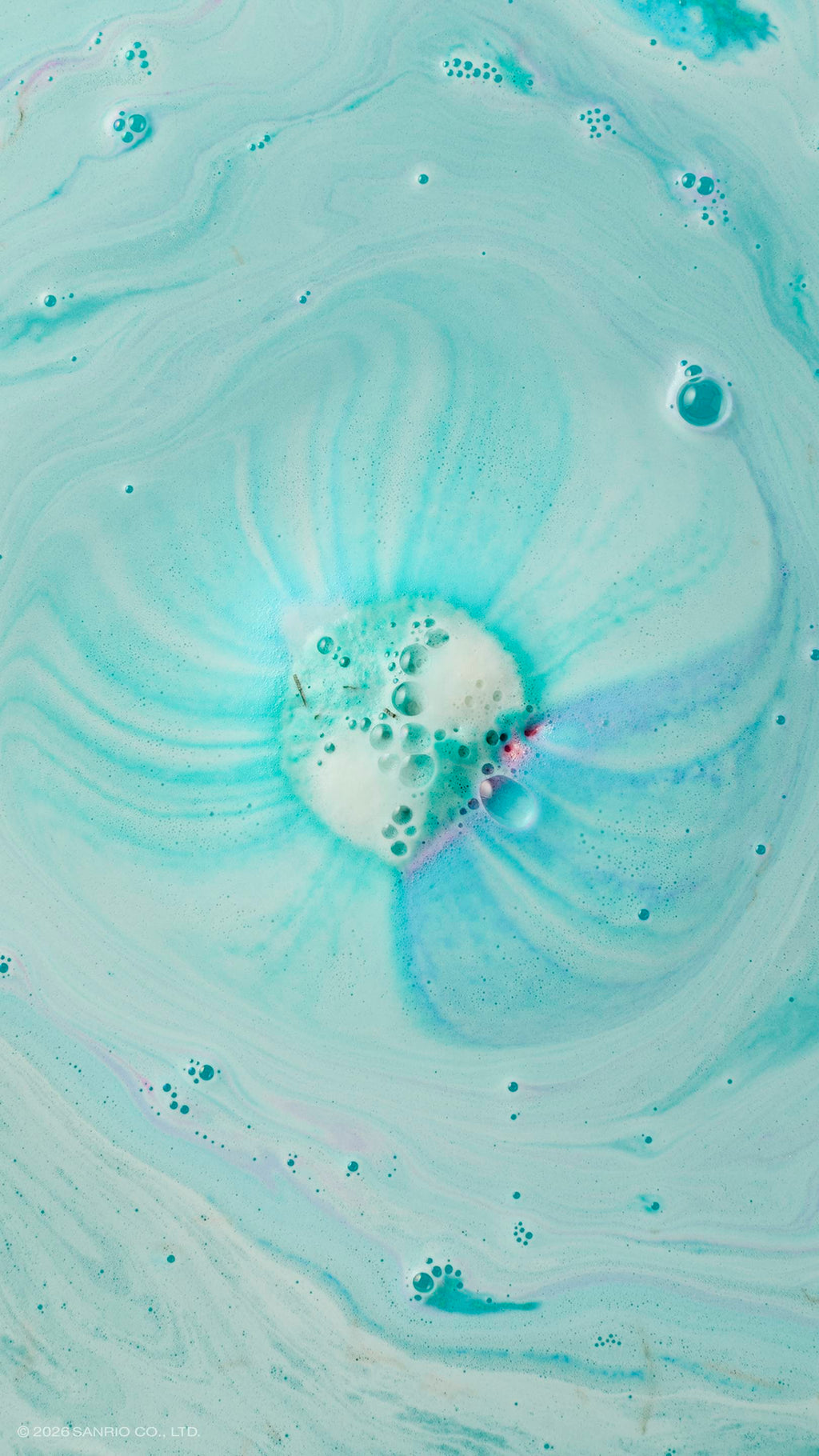 An aerial shot of turquoise bath water swirling with white foam and bubbles. In the centre, a bath bomb has mostly dissolved, leaving behind a circular patch of froth with faint streaks of purple and dark teal radiating outwards.
