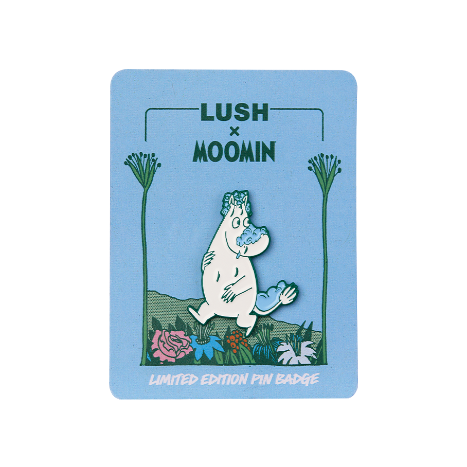 A 'Lush x Moomin' limited edition pin badge on a light blue backing card. The enamel pin depicts Moomintroll walking through colourful flowers with blue soap suds on his nose, head, and tail.