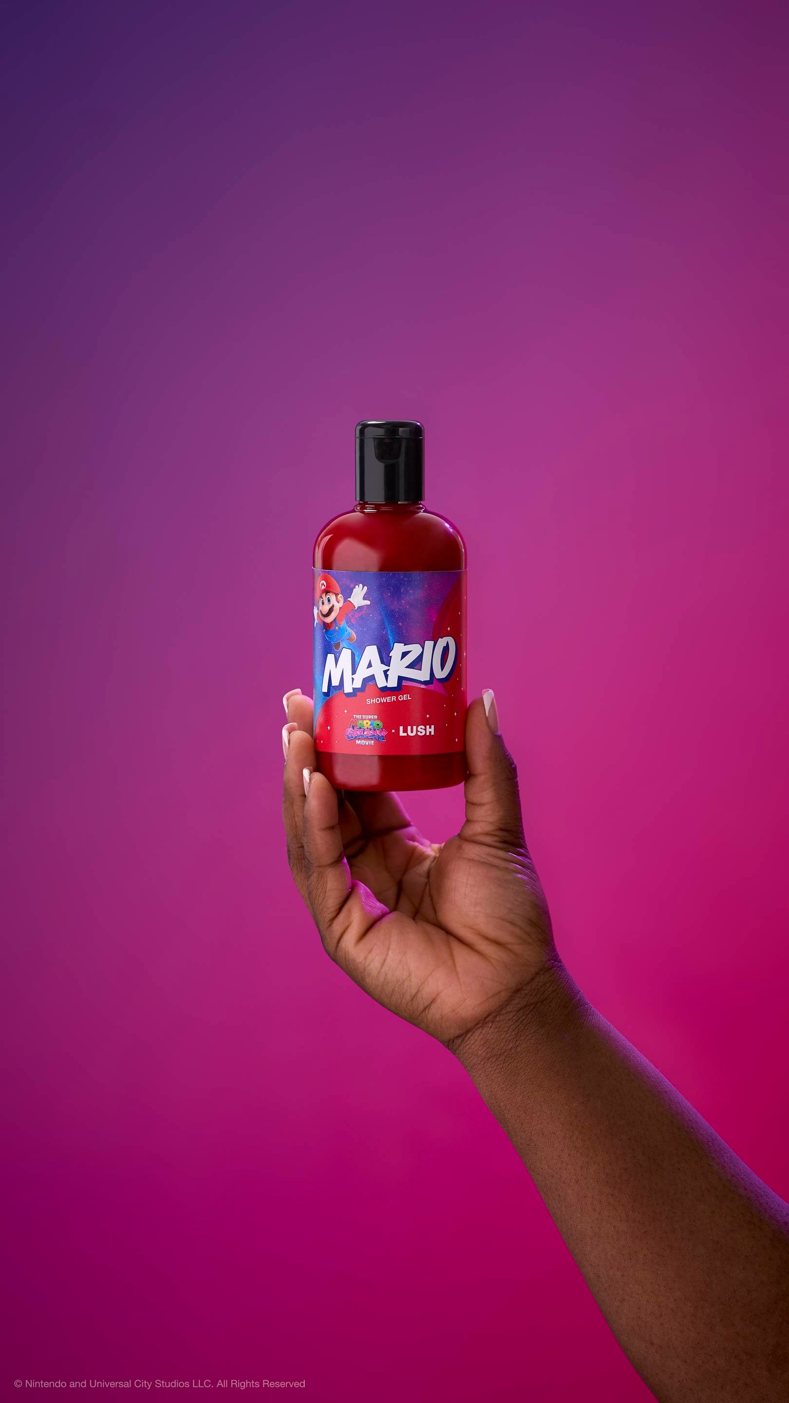 Hand holds a red Mario shower gel bottle with a black cap against a purple-magenta gradient background. The label features Mario jumping against a starry galaxy background with "MARIO SHOWER GEL" in bold letters.
