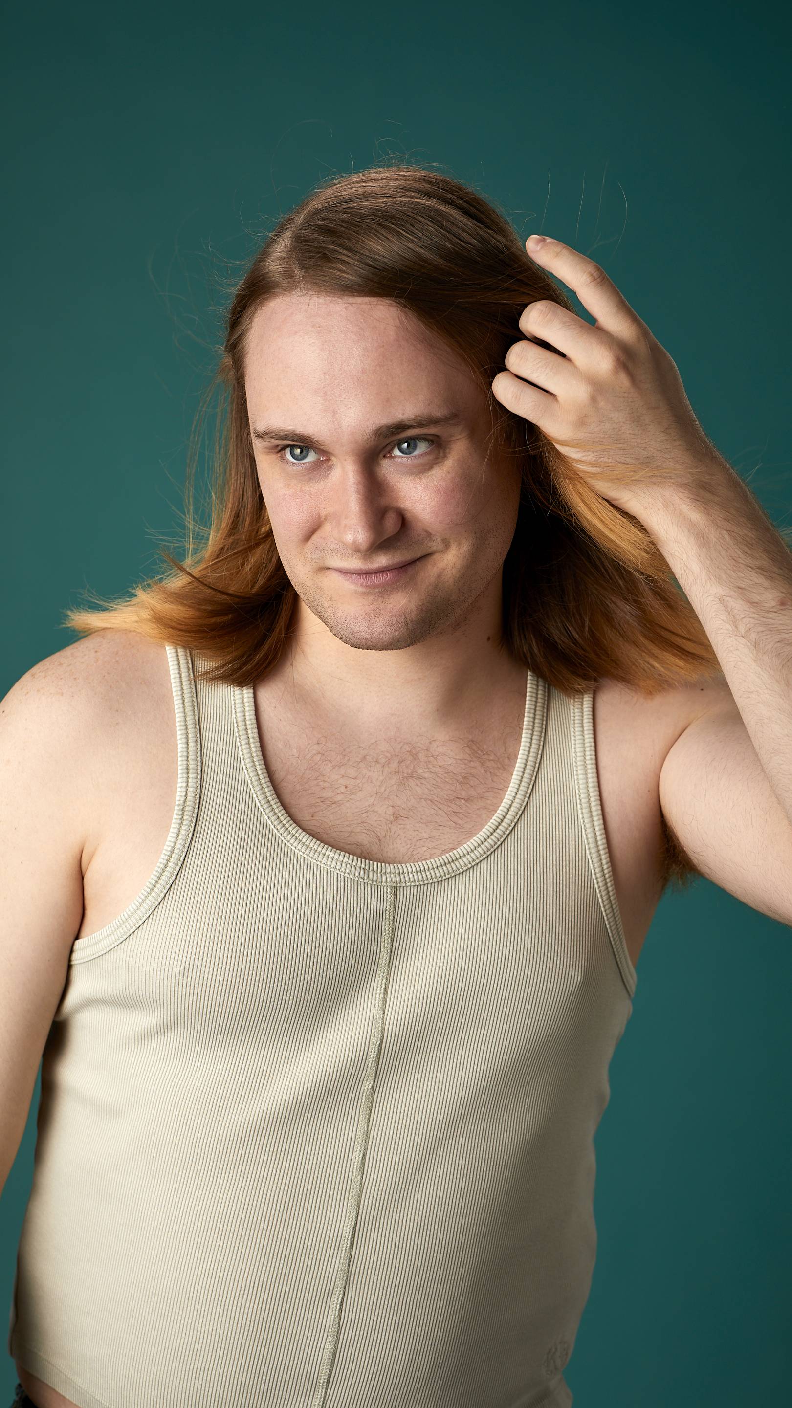 The model is on a teal background with a cream-coloured tank top. They have light brown, shoulder-length, freshly-dried hair which looks shiny and healthy and is being fanned with air.