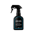 A recycled black plastic LUSH body spray bottle with a trigger nozzle stands upright with a blue rimmed label with white text that reads "Blue Skies and Fluffy White Clouds Body Spray".