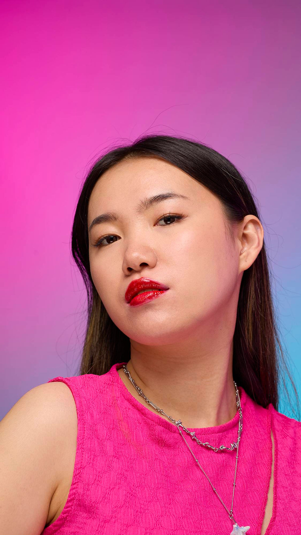 The model has long, straight dark hair and is on a pastel pink, blue and purple hue background. Their make-up has been done with the focal point being the juicy coating of cherry-red tint on their lips created by the Cherry lip jelly.