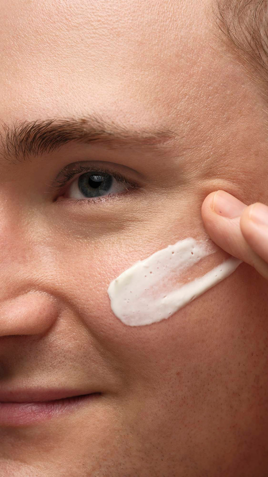 A close-up image of the mode's cheek as they gently smooth the Cosmetic Lad self-preserving moisturiser over their cheekbones.