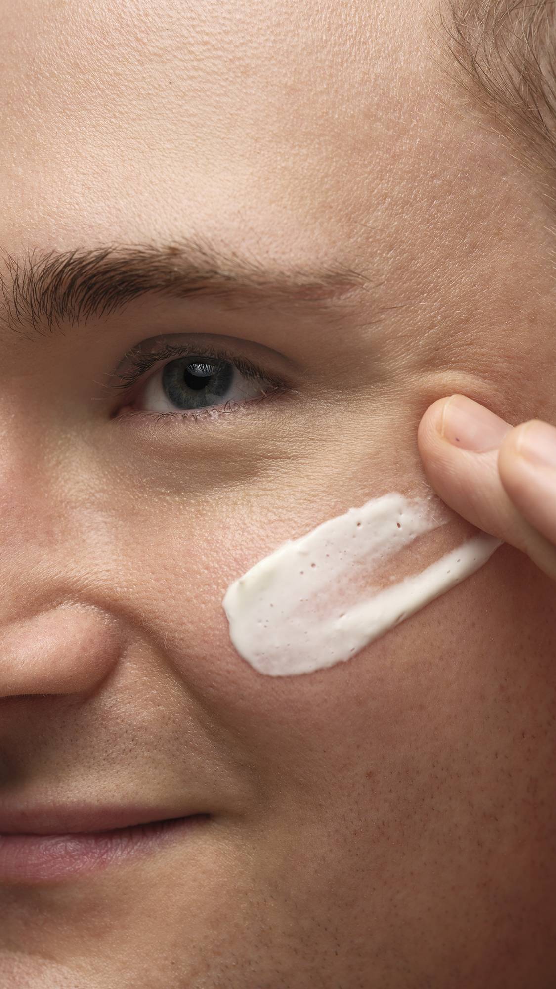 A close-up image of the mode's cheek as they gently smooth the Cosmetic Lad self-preserving moisturiser over their cheekbones.