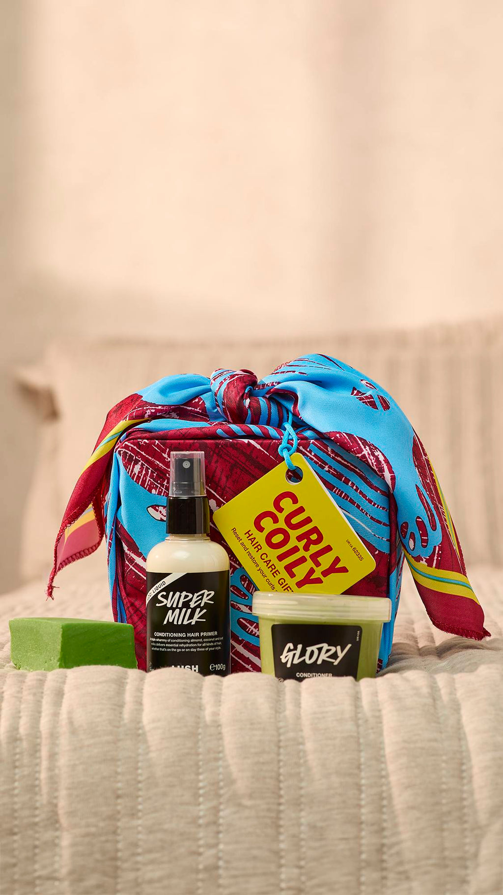 A close-up of the Curly Coily wrapped haircare gift set on the foot of the bed with the three haircare products sitting in front.