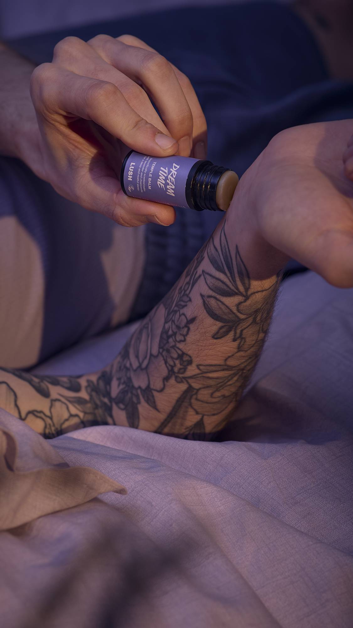 A close-up image of a model's hands as they use the push-up tube of Dream Time temple balm on their wrist.
