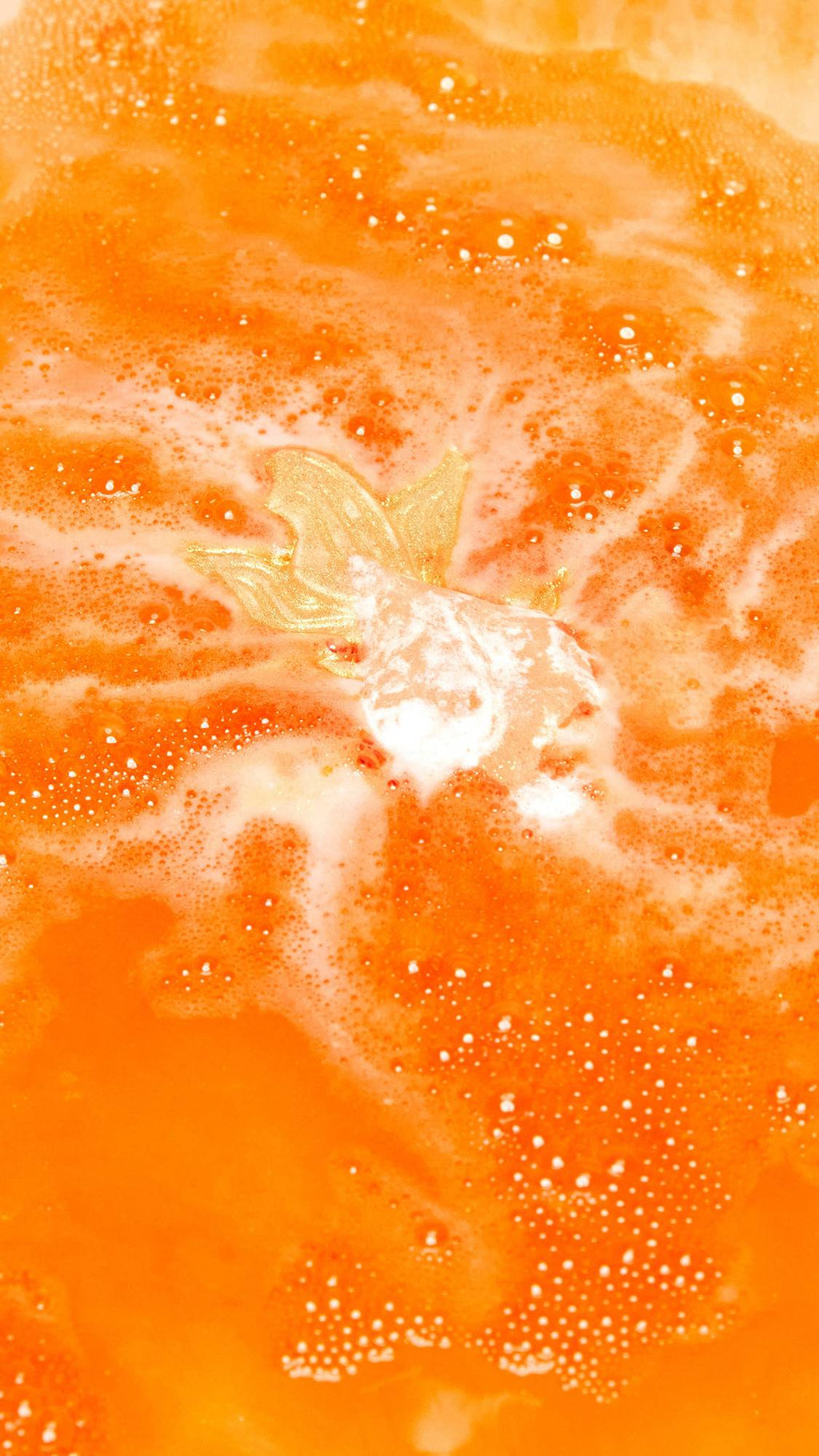 The Goldfish bath bomb is slowly dissolving creating a shimmering sea of deep, sunset-orange water and thick, vibrant foam.