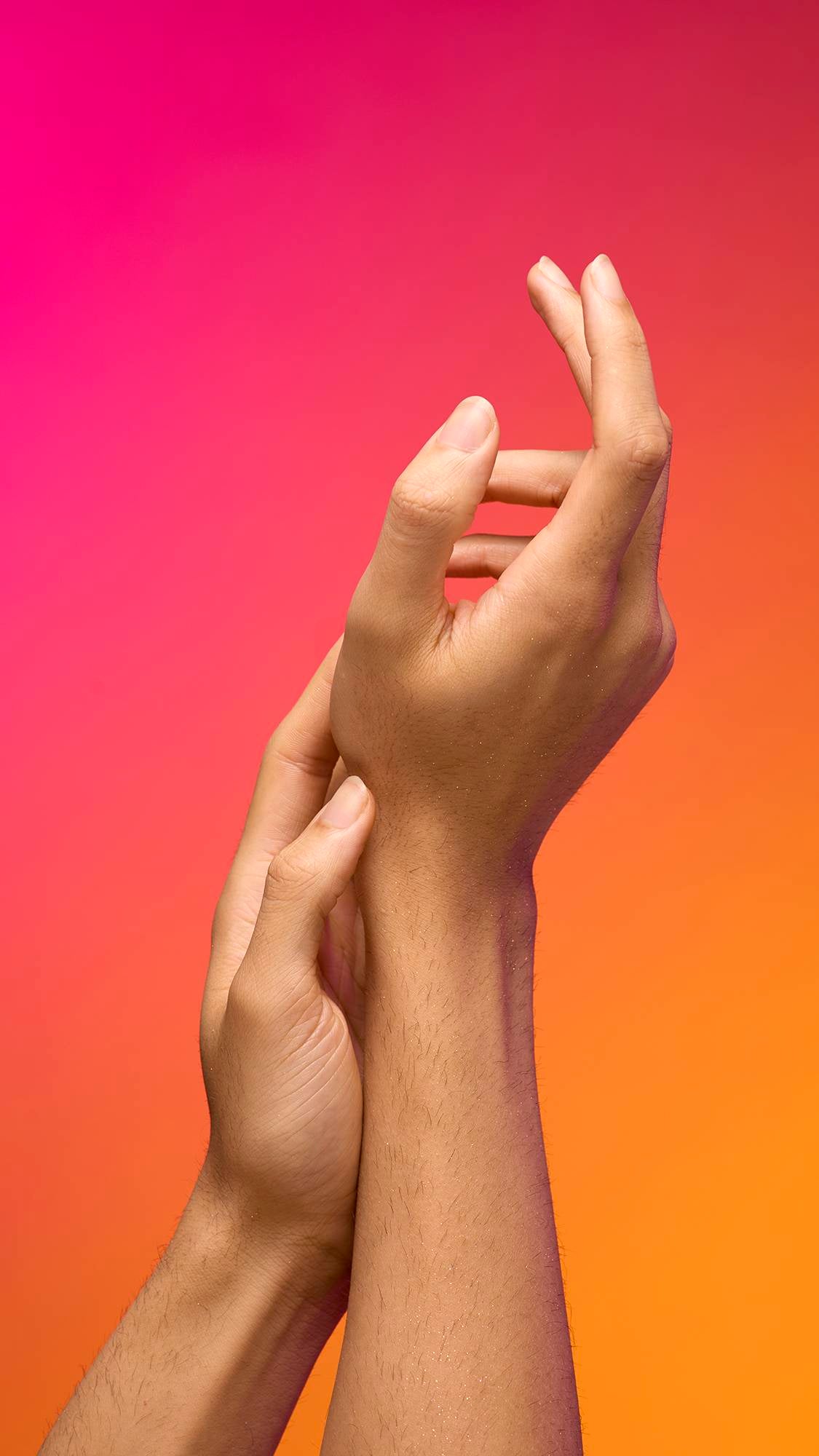 The image shows a model's forearm extended from the left-hand side as the skin appears moisturised with a subtle, delicate shimmer over the skin after having used the Intergalactic Glitter Mist spray product on a pink-to-orange gradient background.