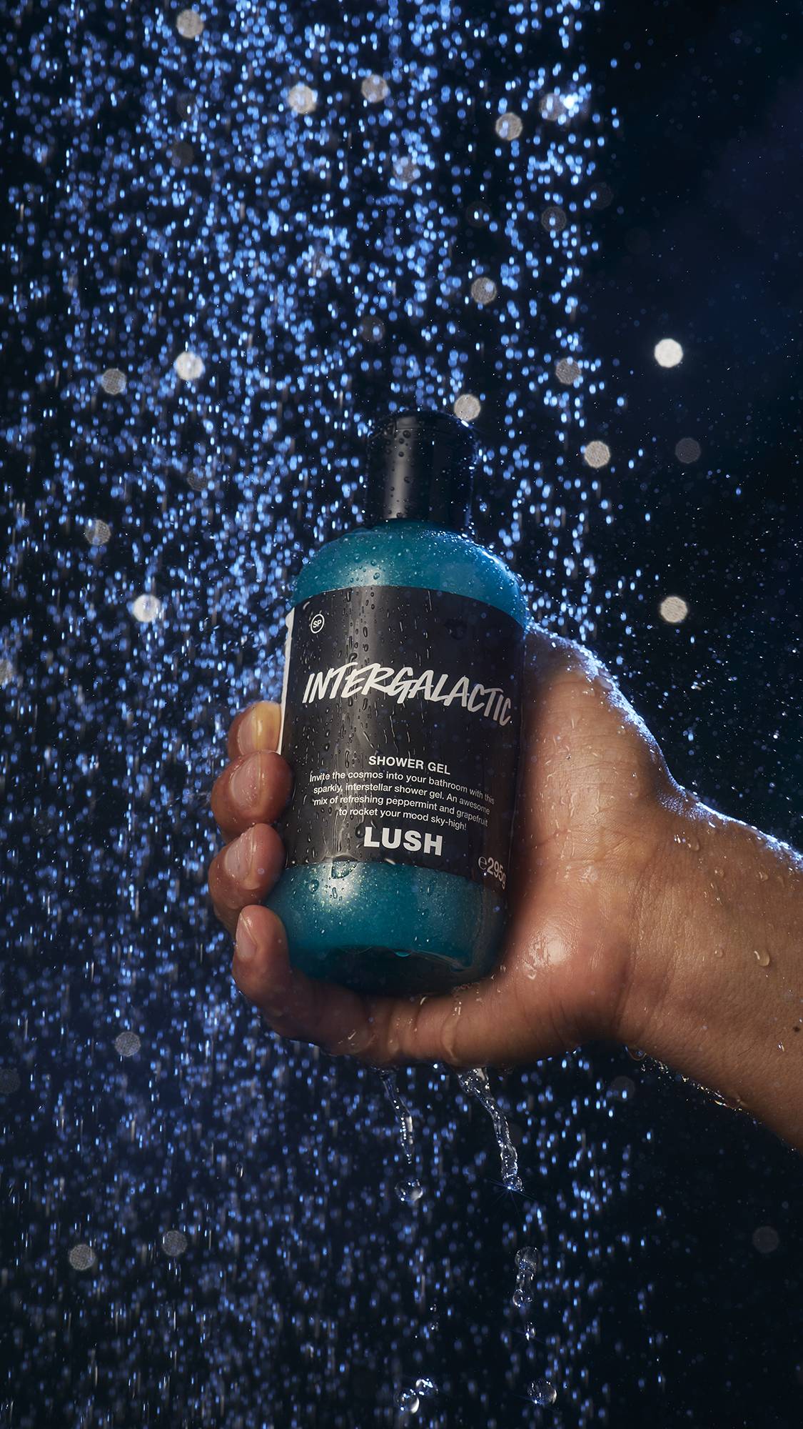 Image shows a model holding a bottle of the shower gel under a shower.