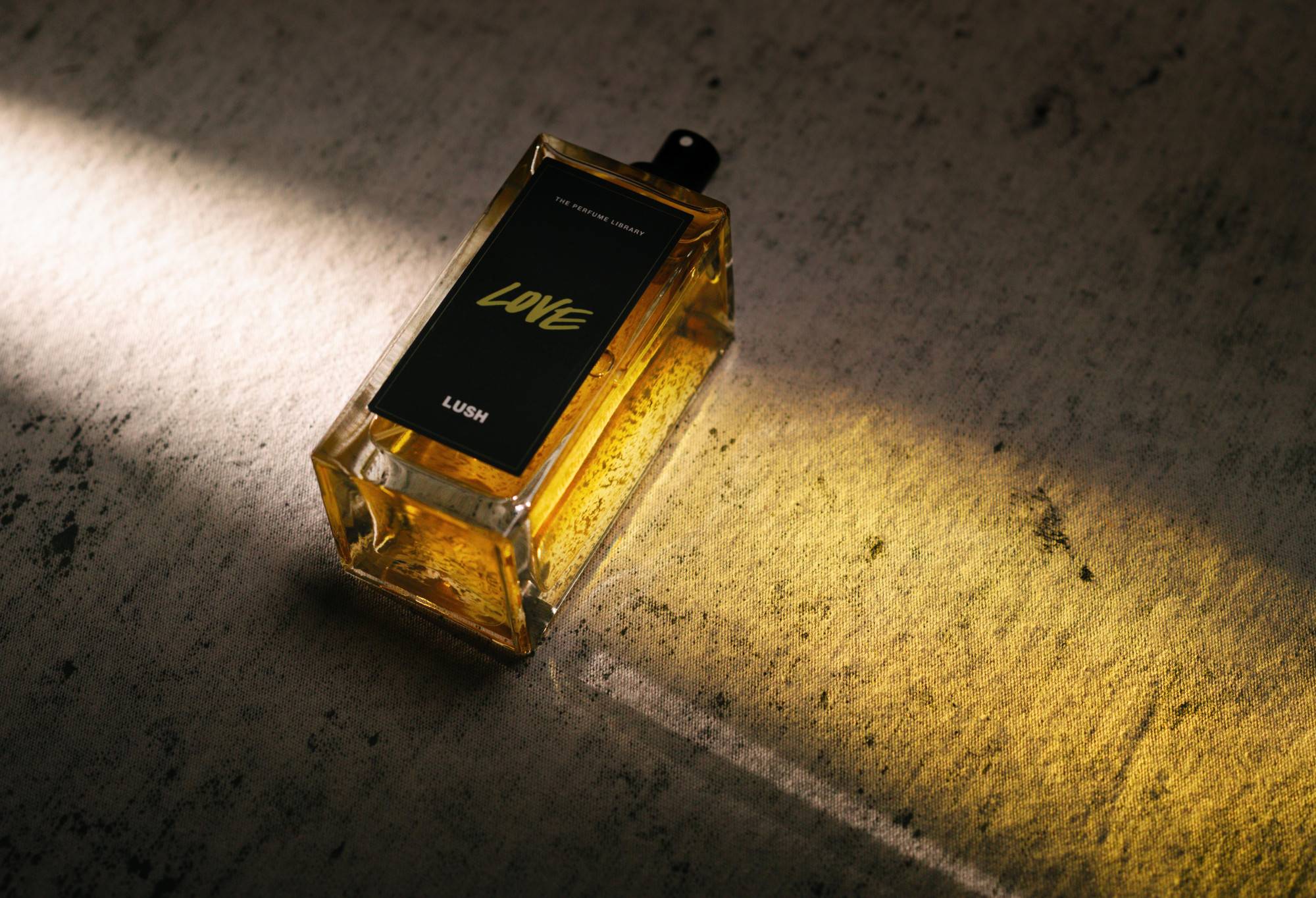 Love, a bottled, black label perfume, lies flat, with light shining through it, creating a golden cast of light.
