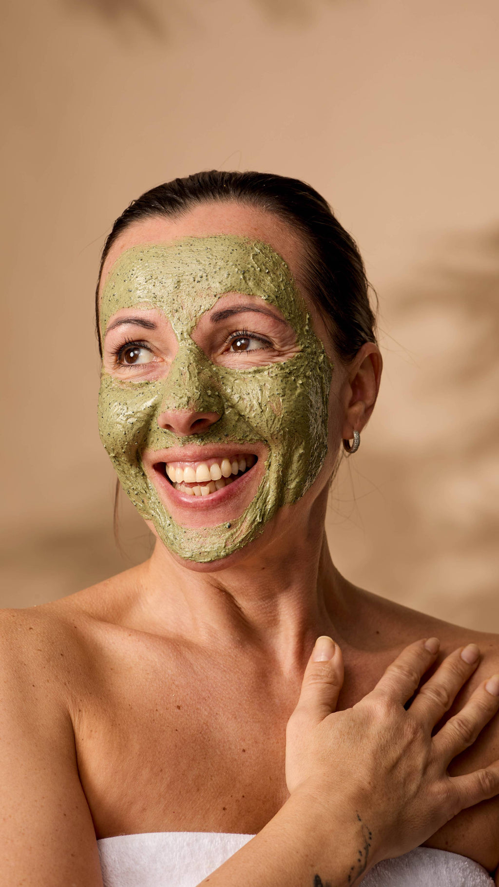 The model is wrapped in a fluffy white towel and their face is evenly covered in the Matcha face mask.