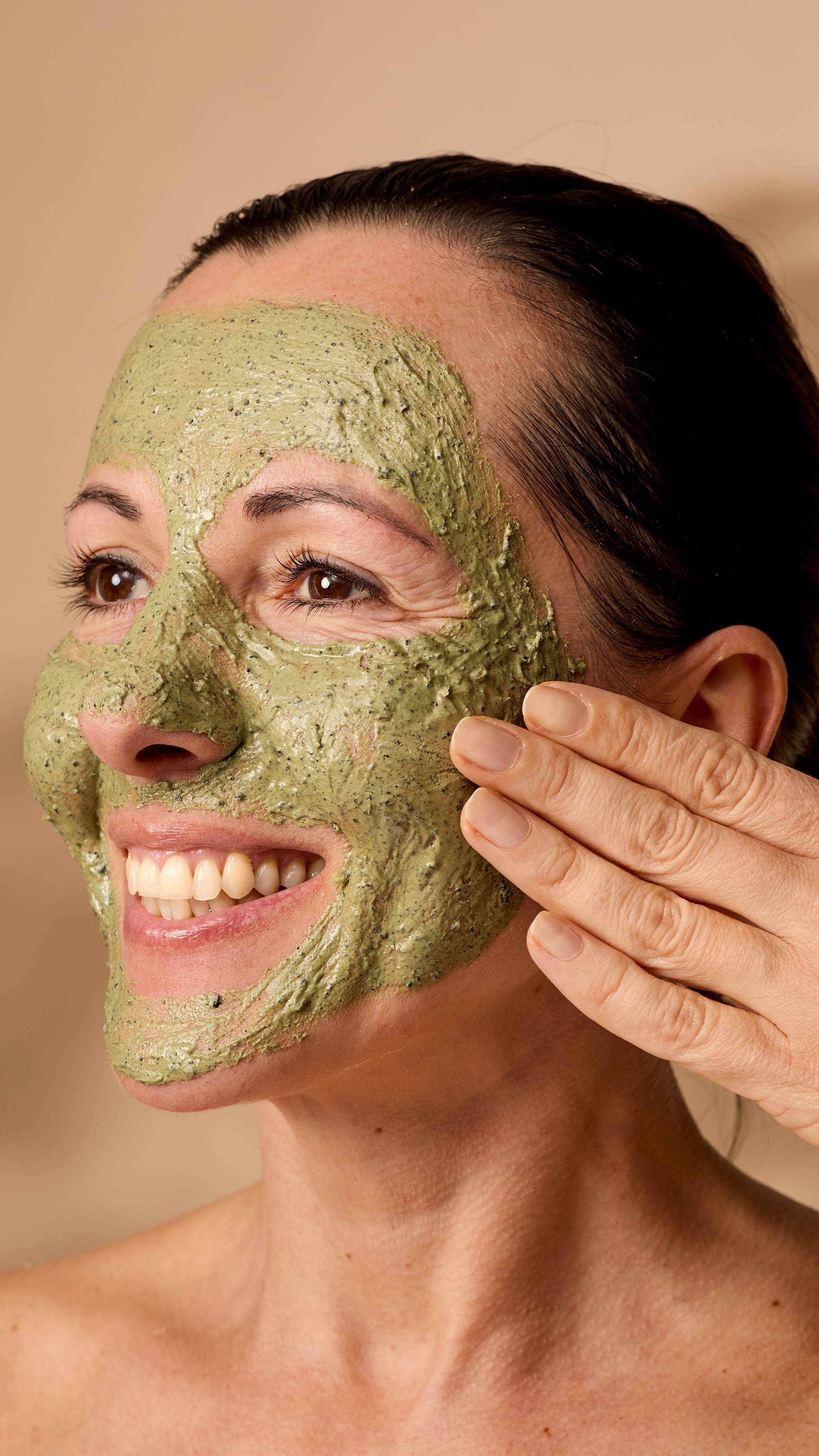 A close-up of the model's smiling face as they showcase the deep green textured Matcha face mask.
