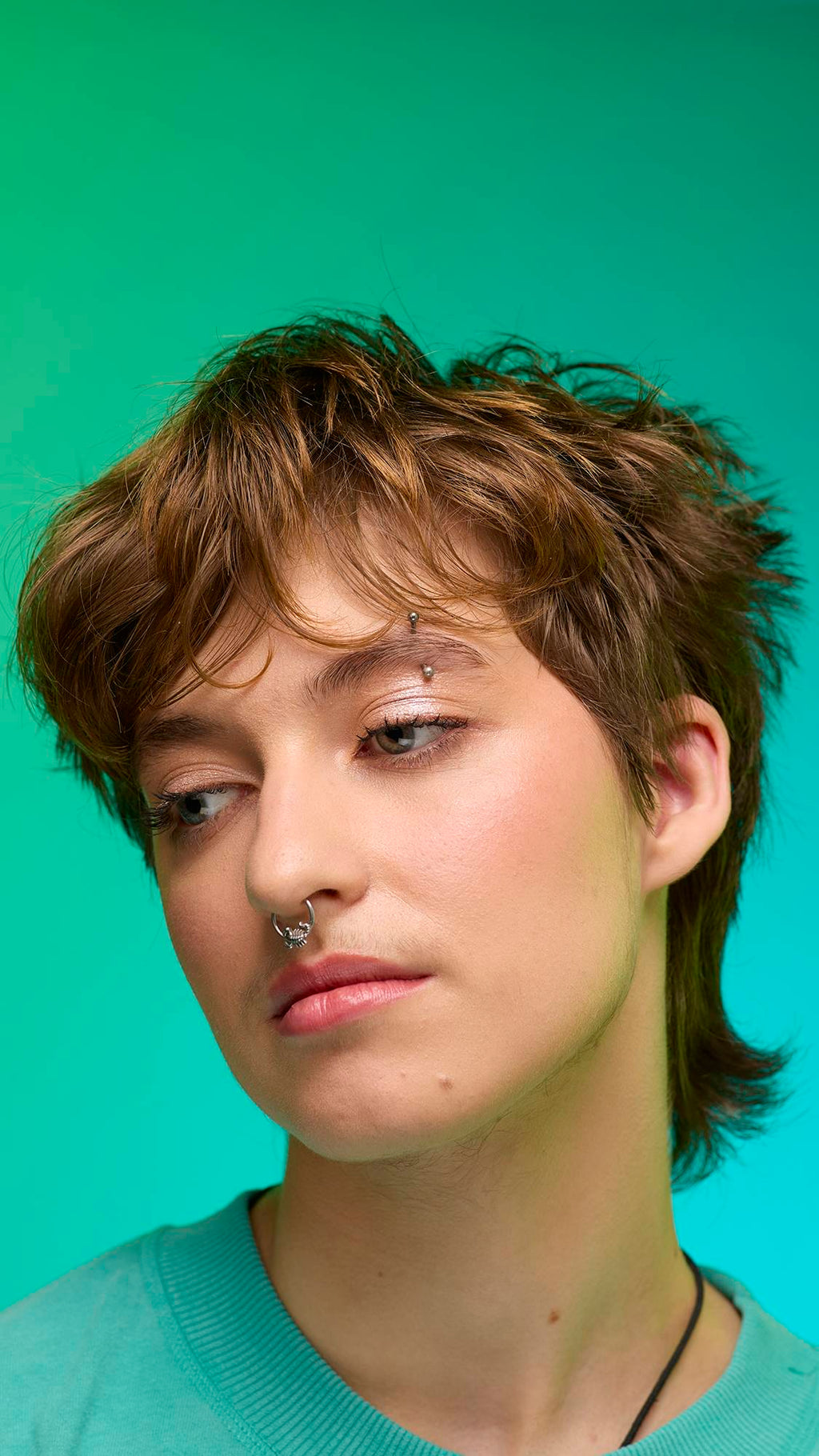 The image shows a close-up of the model's face on a pale blue-to-green gradient background. The model's make-up is done with the focal point being a subtle, iridescent, shimmering eyeshadow made by the New Moon Glitter Crumble.