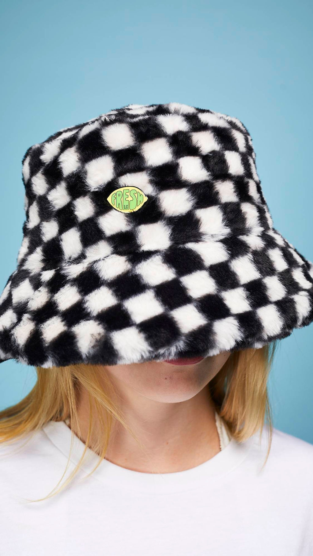 A super close-up of the model's face and head wearing a black hat with the Fresh Values pin badge attached.