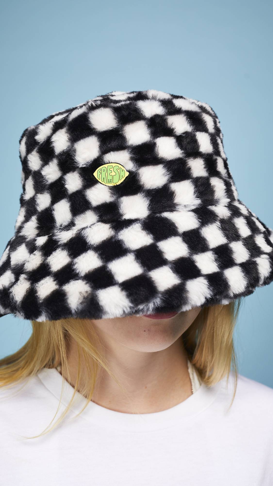A super close-up of the model's face and head wearing a black hat with the Fresh Values pin badge attached.
