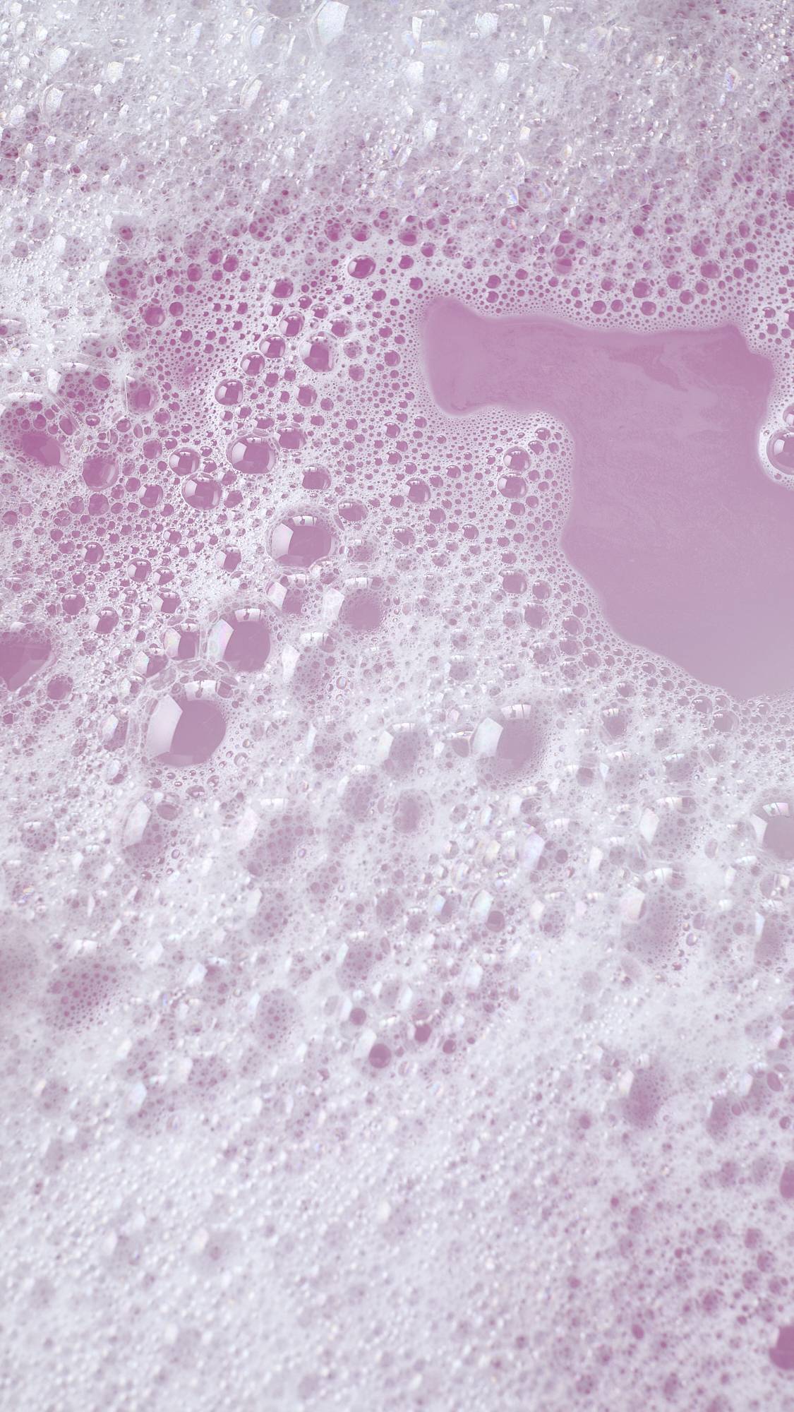 The image shows the colourful aftermath of using the Pink Flamingo reusable bubble bark stick. There is delicate, rose-pink bath water surrounded by mountains of bright bubbles.
