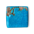 Rub Rub Rub. A cube-shaped, vibrant turquoise product. One corner features a rough brown patch with salt crystals. The blue surface is smooth with tiny flecks.