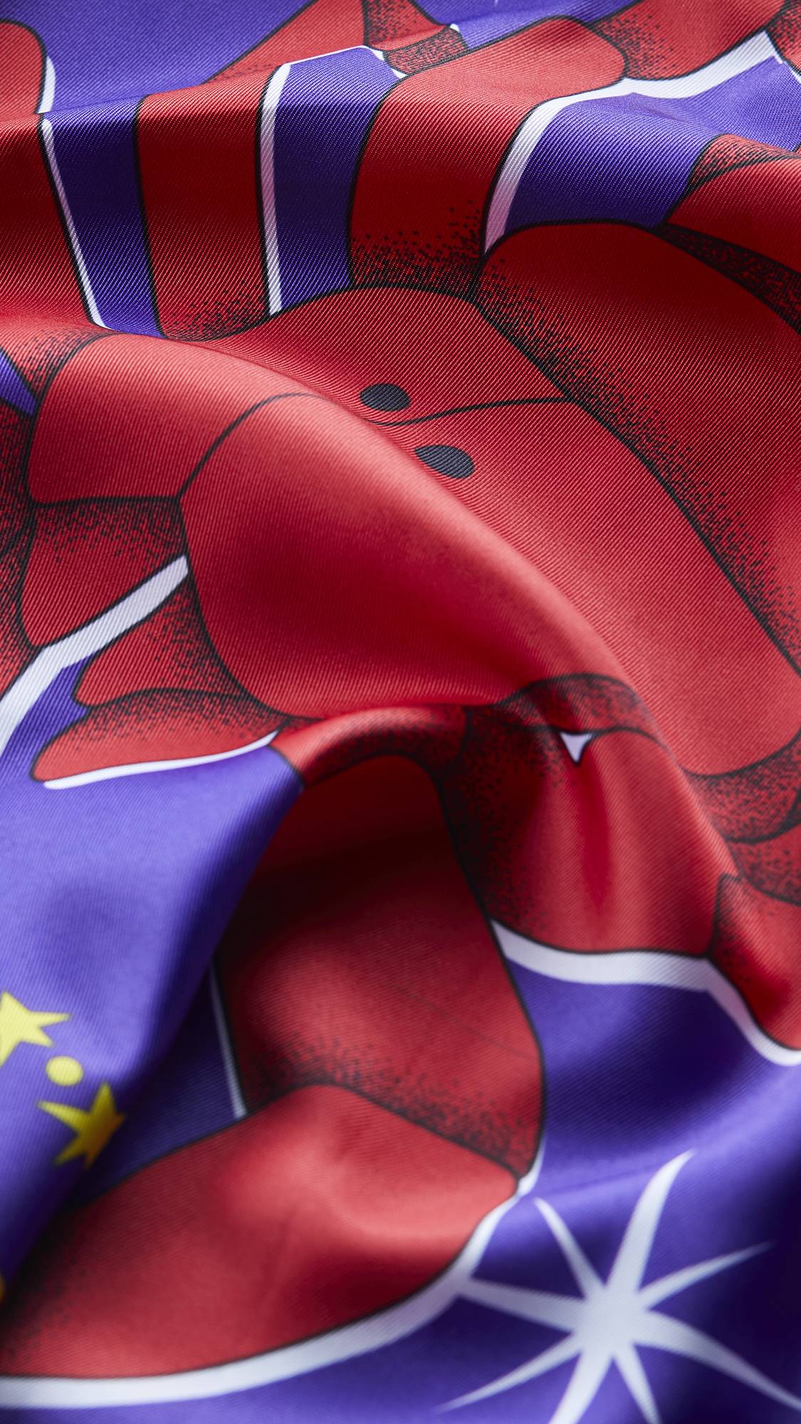 The image shows a super close-up of the Scorpio knot wrap as it lays ruched. The image focuses on the texture of the fabric and the vibrant contrasting colours of reds and purples.
