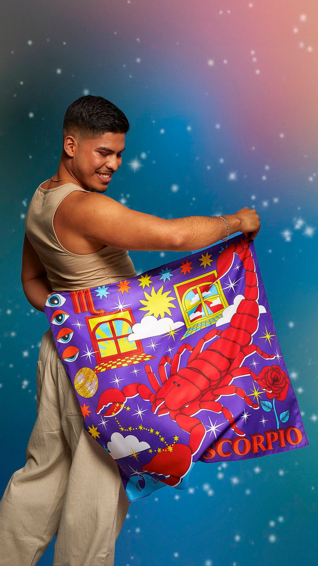 The image shows the model wearing a beige tank top and linen trousers. They are facing away on a pastel, sparkling background and holding the Scorpio knot wrap behind their back showing the full design.