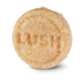 Honey I Washed My Hair. A round, textured, pale beige Lush solid shampoo bar. The bar has a rough, shredded-coconut texture and is embossed with the "LUSH" logo in the centre.