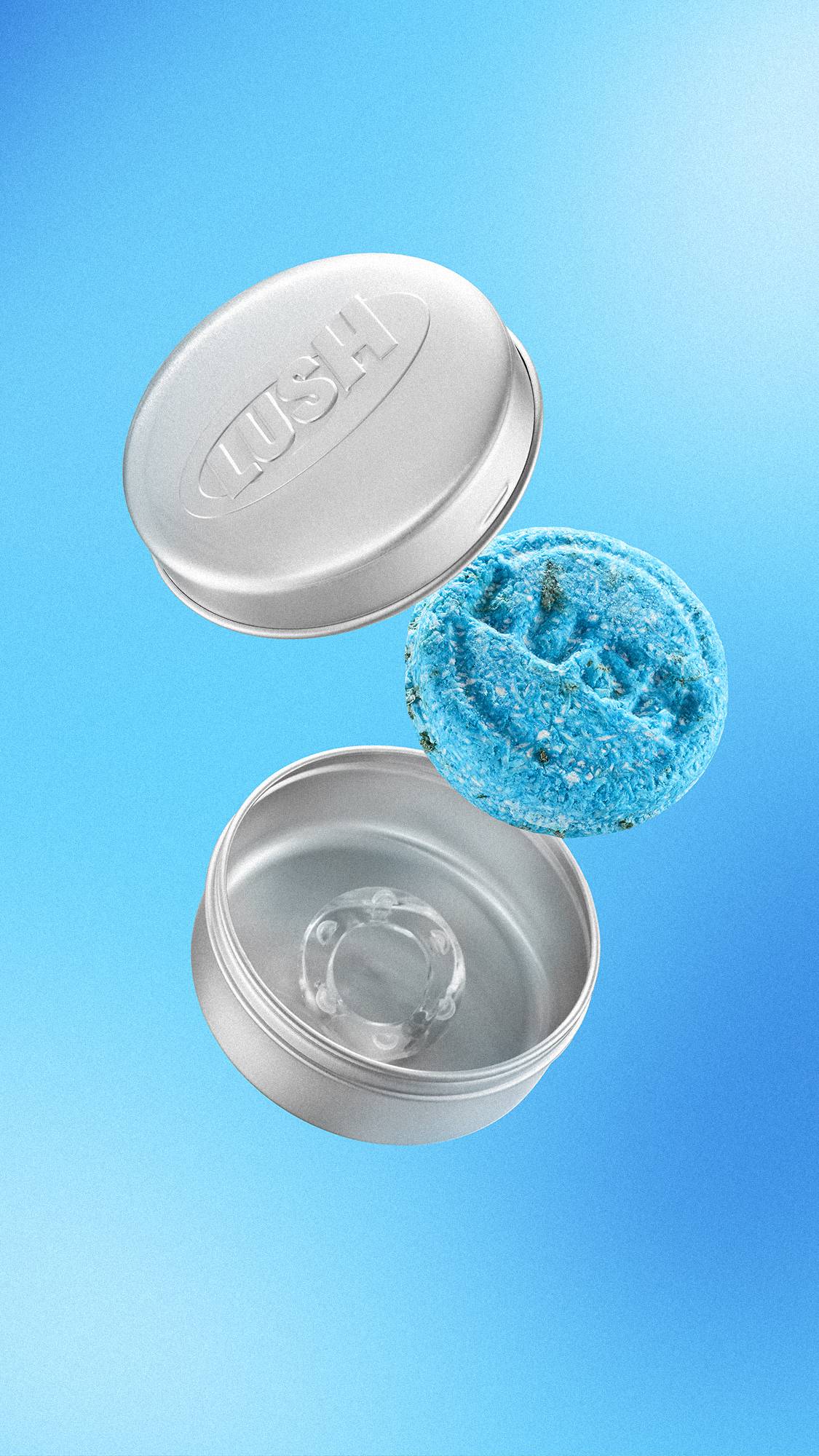 A textured, bright blue "Seanik" solid shampoo bar floats in mid-air between the lid and base of an open, silver aluminium Lush tin. The lid features an embossed 'LUSH' logo. Set against a light-to-mid blue gradient background.