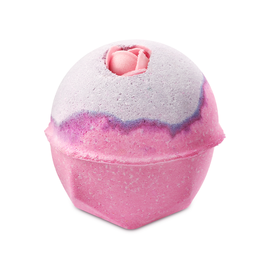 The Sex Bomb Bath Bomb features a vibrant pink lower half and a soft, pale purple top, separated by a thin, darker purple line. A delicate pink rosebud is nestled into the very top of the sphere, adding a romantic touch.