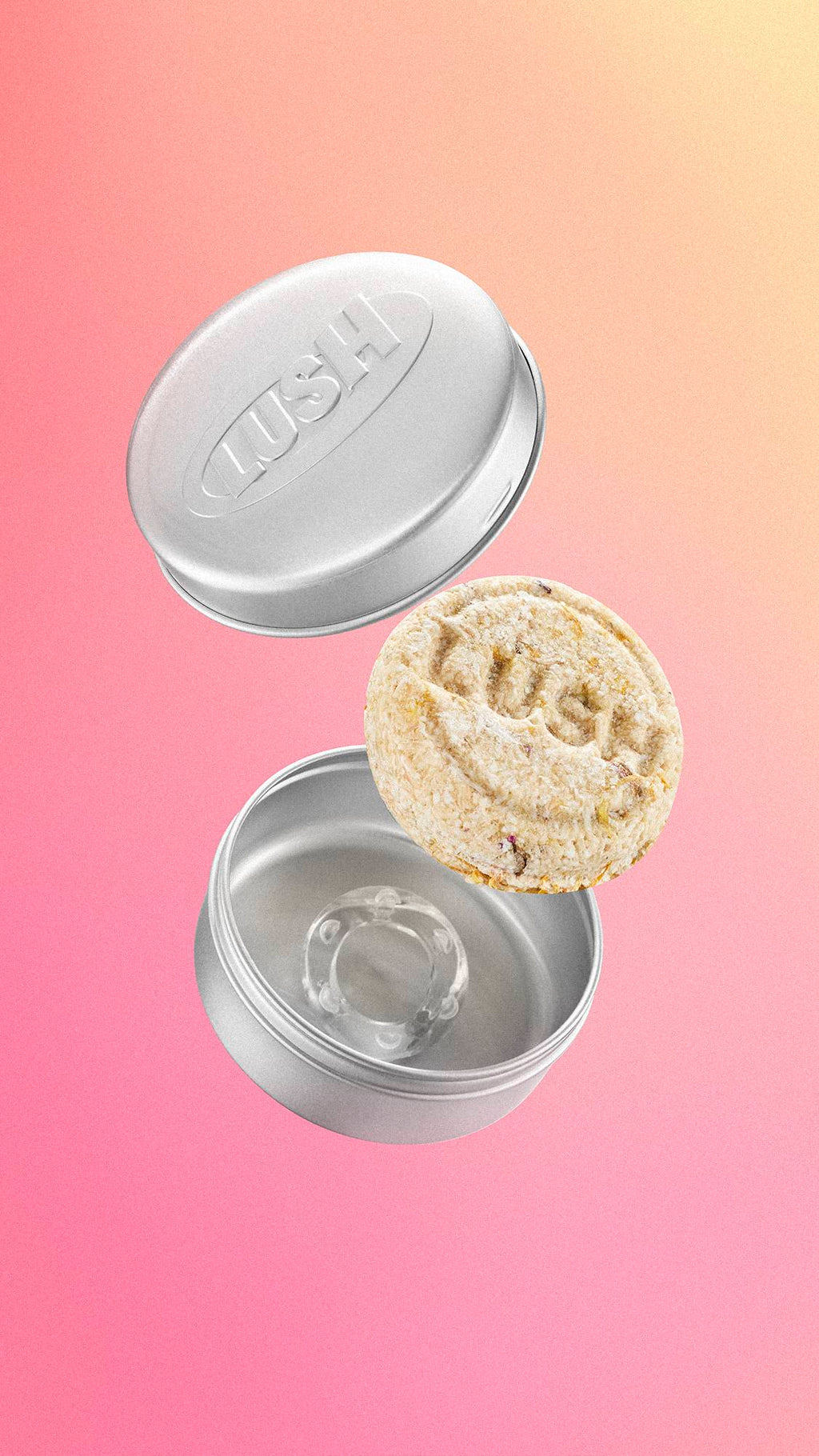A circular, textured cream Lush shampoo bar floats mid-air between an open, embossed silver aluminium storage tin and its lid. The items are suspended against a soft, smooth pink and yellow gradient background.
