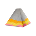 Volcano. A grey, pyramid-shaped bath bomb-style foot soak. The base features layered, wavy bands of vibrant orange, yellow, and bright pink, creating a colourful contrast against the neutral grey upper half.