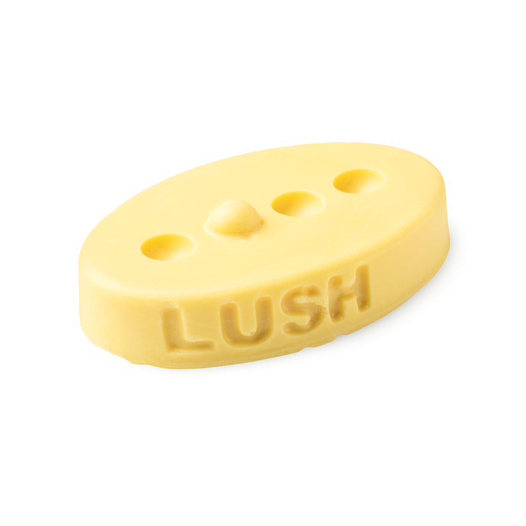 Therapy. A buttery yellow, oval shaped, solid massage bar, with a design of 3 small holes cut out with 1 bump in a line.