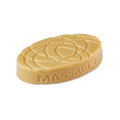 An oval, smooth caramel-coloured Lush "Turmeric Latte" massage bar features a geometric, indented pattern across its top surface. The words MASSAGE BAR are embossed along the curved edge.