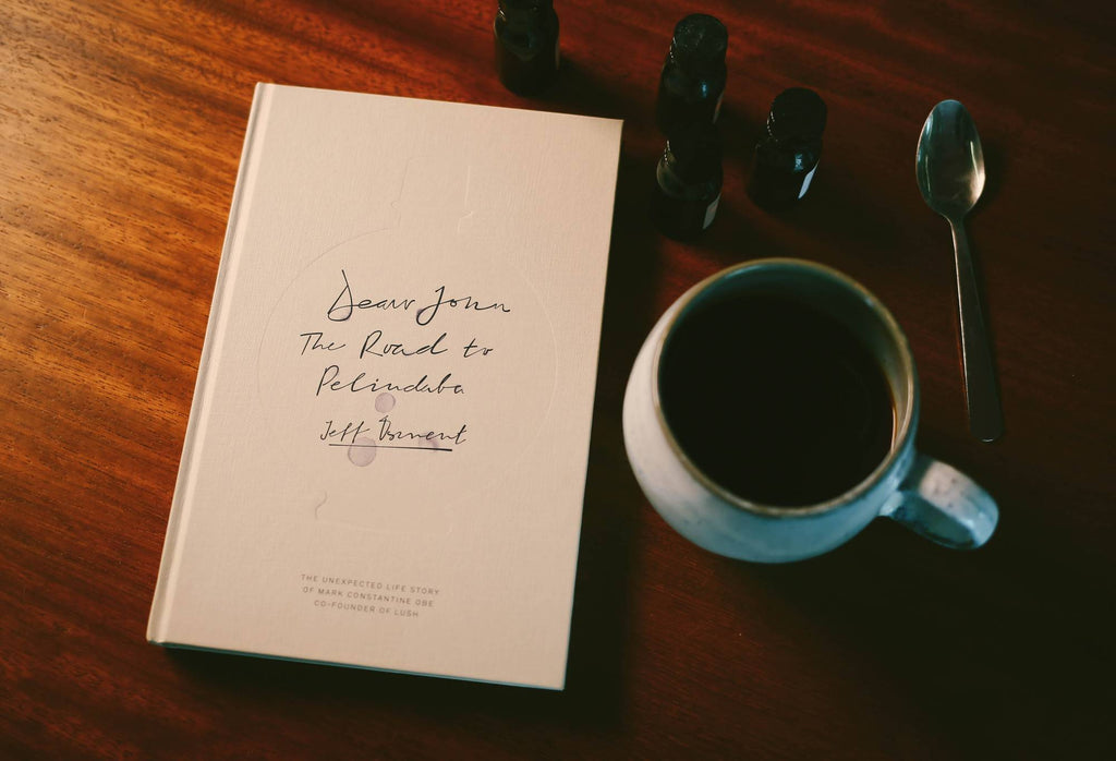 The book presented at an angle on a wooden surface. Placed next to a drinking cup, a spoon and aromatherapy bottles.